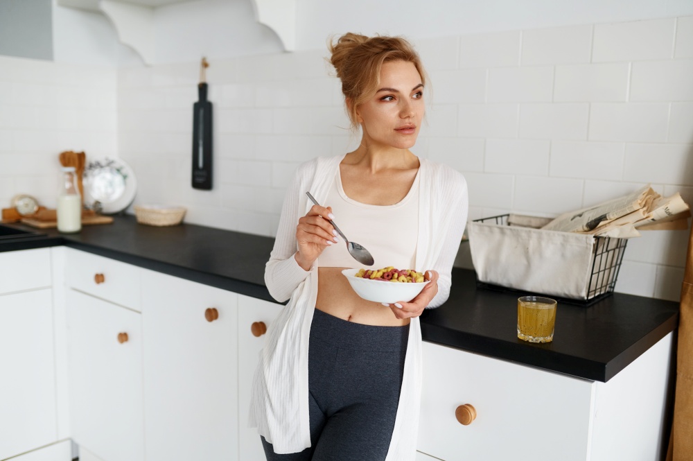 Dreamy young woman eating cereals with milk healthy breakfast on home kitchen after morning fitness training workout. Dreamy young woman eating cereals with milk on home kitchen