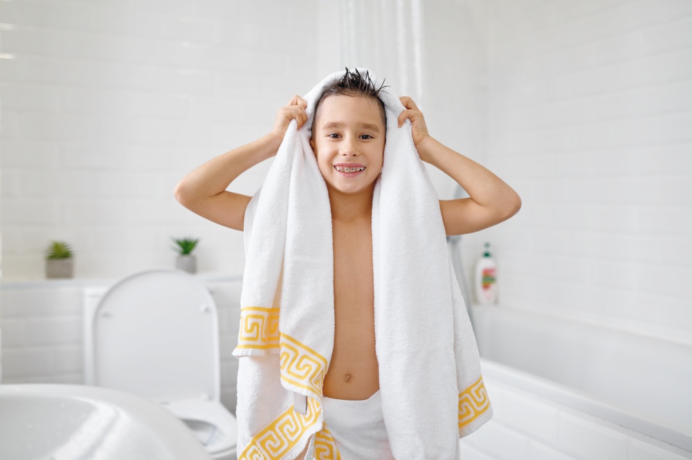 Portrait of happy boy wrapped in white towel showing toothy smile with dental braces after bath or shower. Children morning hygiene routine. Portrait of happy boy wrapped in white towel after bath