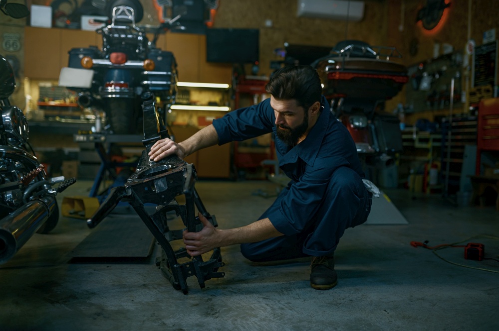 Young hipster man mechanic repairing motorcycle in workshop working with frame. Repairman checking and diagnosing parts on motorbike. Young hipster man mechanic repairs motorcycle in workshop working with frame