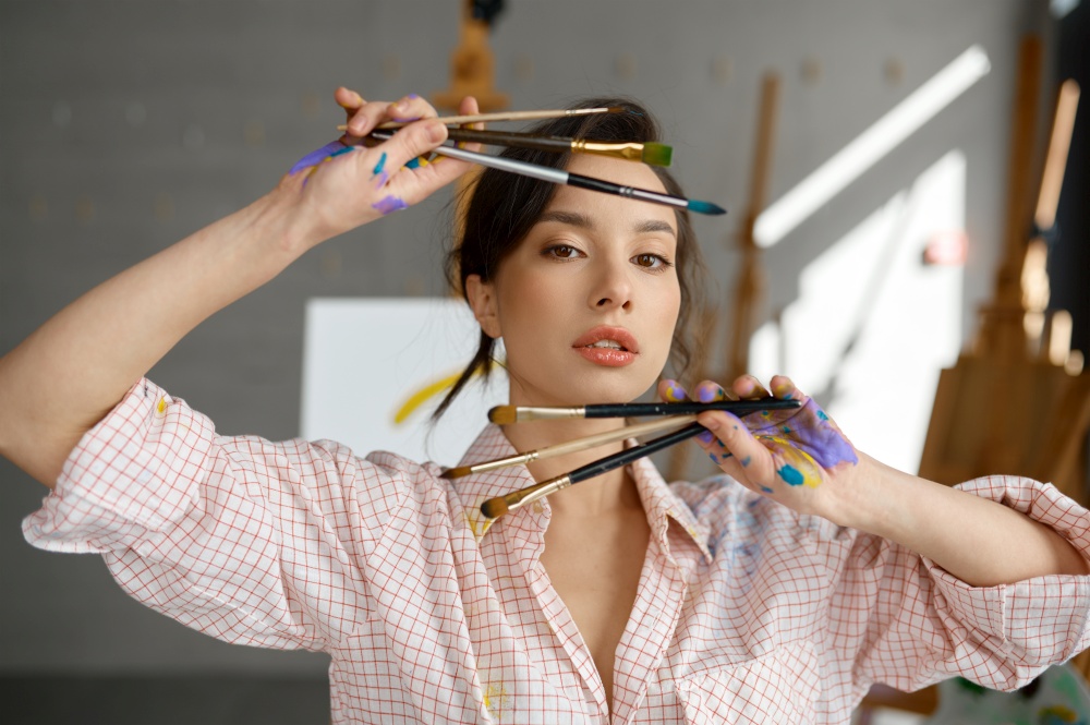 Art portrait of creative female artist with selective focus on dirty painted hands holding bunch of paintbrush. Cropped closeup shot of young painter. Art portrait of creative female artist showing hand with paintbrush