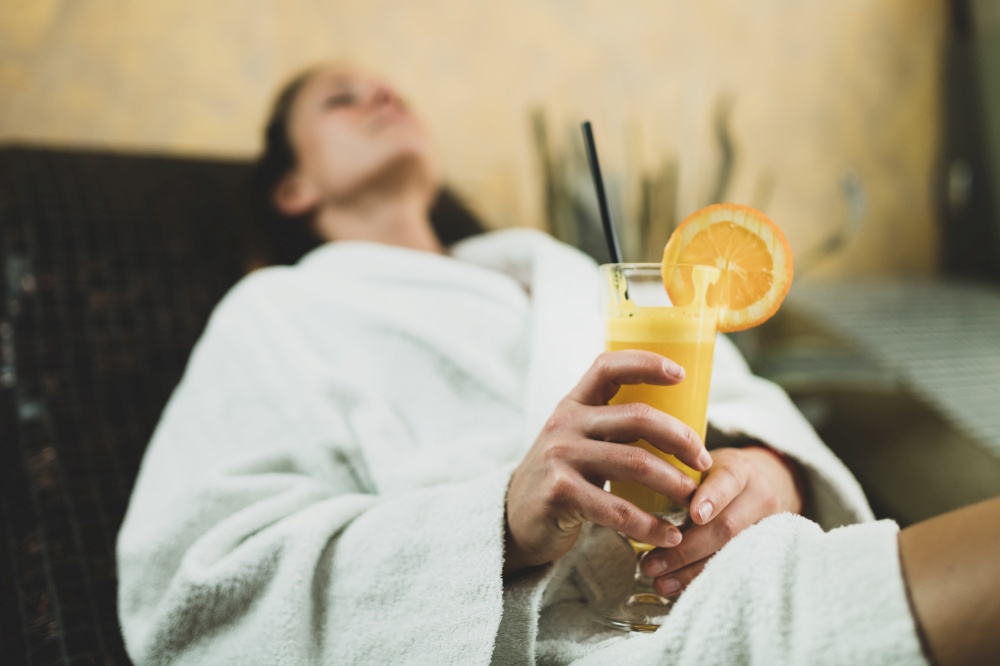 Woman in Bathrobe Lying on Tepidarium Bed and Drinking Lemonade. . Woman Relaxing on a Warm Tepidarium Bed