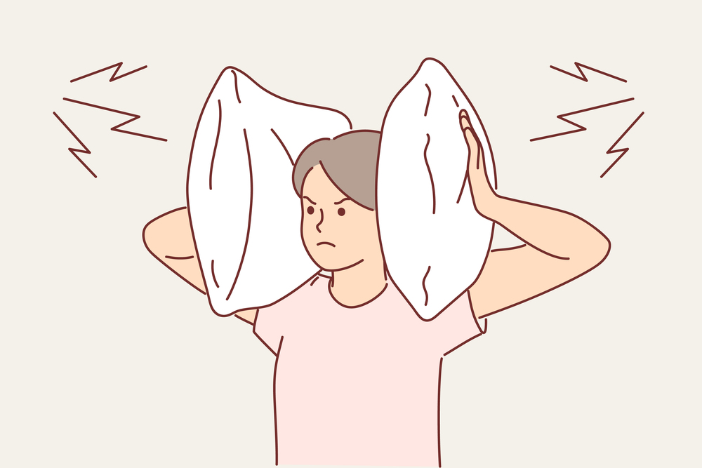 Irritated woman covers ears with pillow so as not to hear noise from neighbors who are having party. Gloomy girl tries to escape from loud music that interferes with sleep and closes ears. Irritated woman covers ears with pillow so as not to hear noise from neighbors who are having party