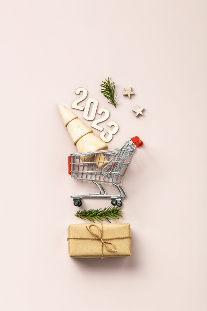 Holiday shopping 2023 concept. Miniature Christmas tree in shopping trolley cart on pink background