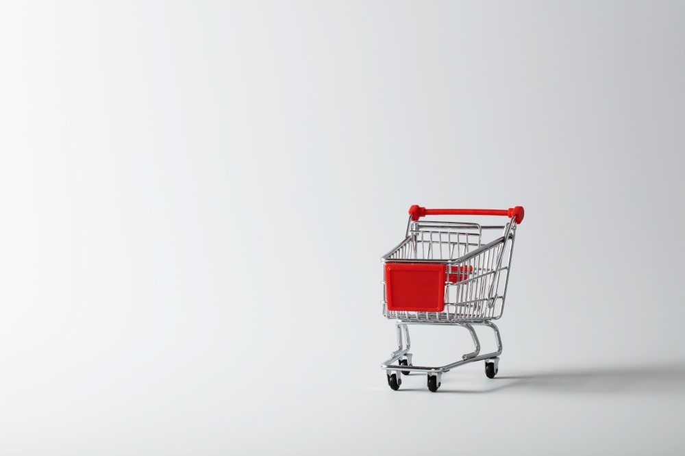Metallic shopping cart trolley on white (off white) background with copy space. Sale, discount, shopping, delivering service concept