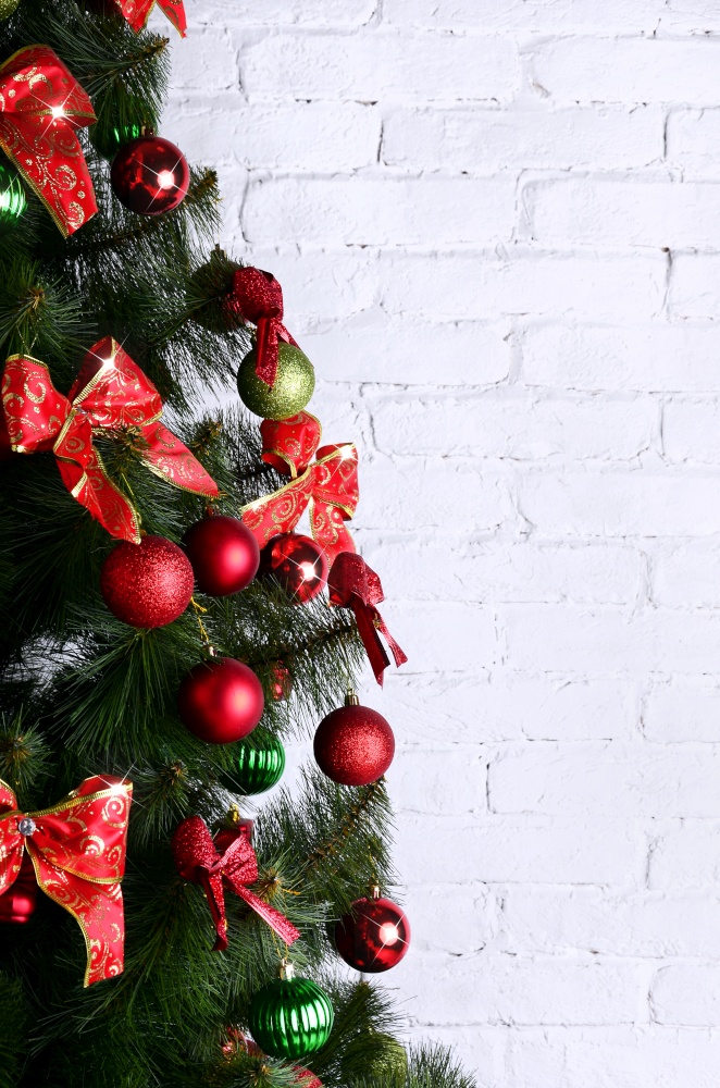 Detailed photo of the Christmas tree decorated with gifts, bright colored spherical toys, ribbons and garlands close-up. Abstract background for Christmas with copy space cards or New Year leaflets. Detailed photo of the Christmas tree on white brick wall