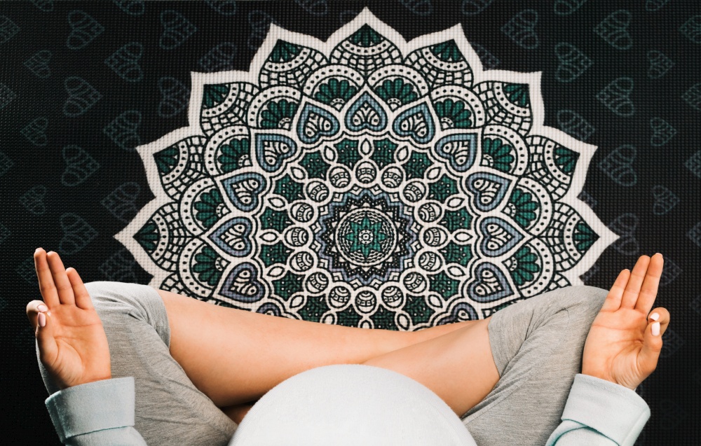 Pregnant woman sitting in lotus position on mandala yoga mat and meditating. Top view.. Pregnant woman sitting in lotus position on mandala yoga mat and meditating. Top view