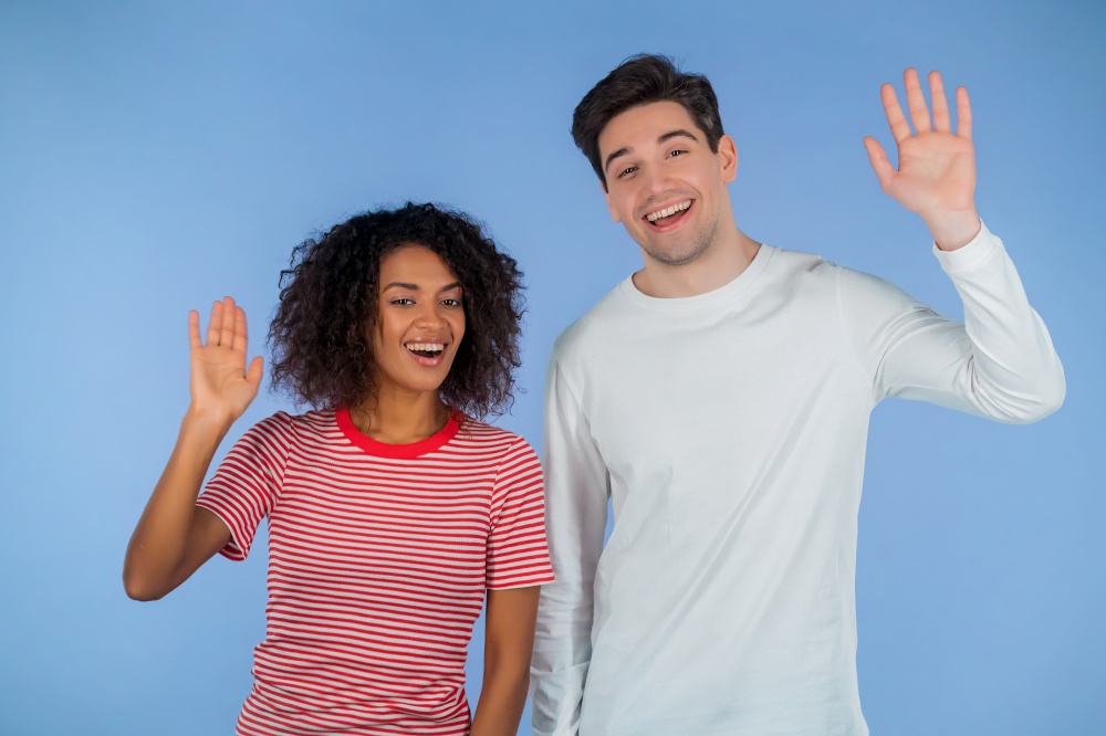 Interracial friendly couple - white man and african woman waving hands - goodbye, chao, adios. Parting, say bye to camera on blue studio background. High quality. Interracial friendly couple - white man and african woman waving hands - goodbye, chao, adios. Parting, say bye to camera on blue studio background.