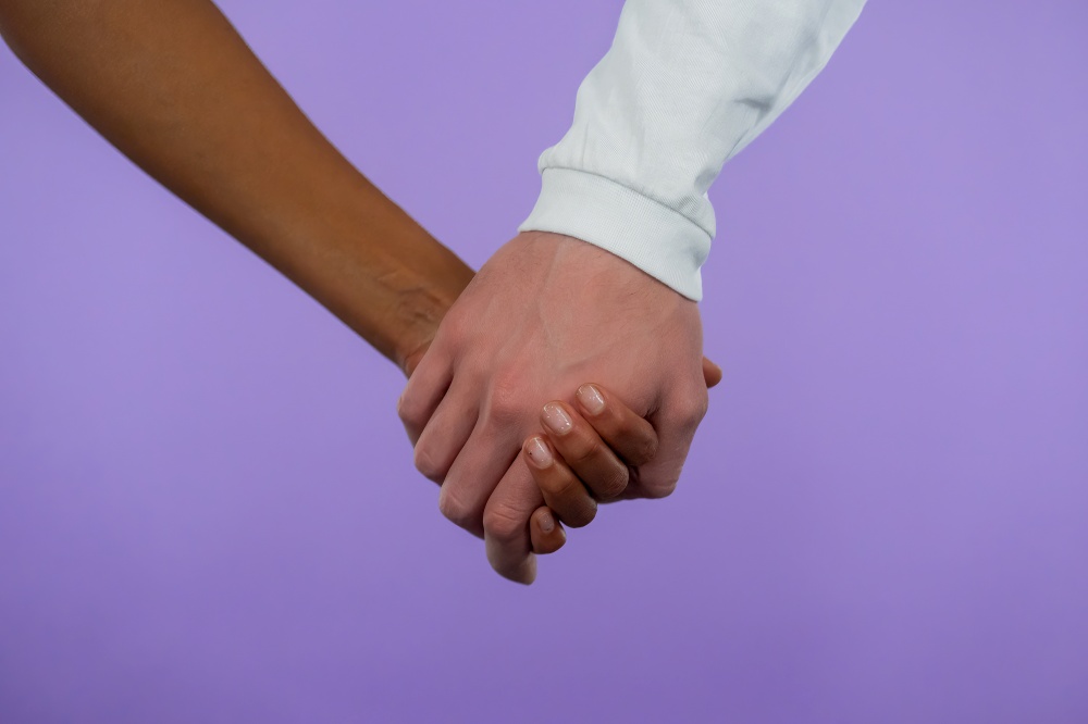 Hands of mixed race woman and white man. Interracial friendship, anti-racism, fraternity. Agreement, cooperation concept on purple background. Hands of mixed race woman and white man. Interracial friendship, anti-racism, fraternity. Agreement, cooperation concept