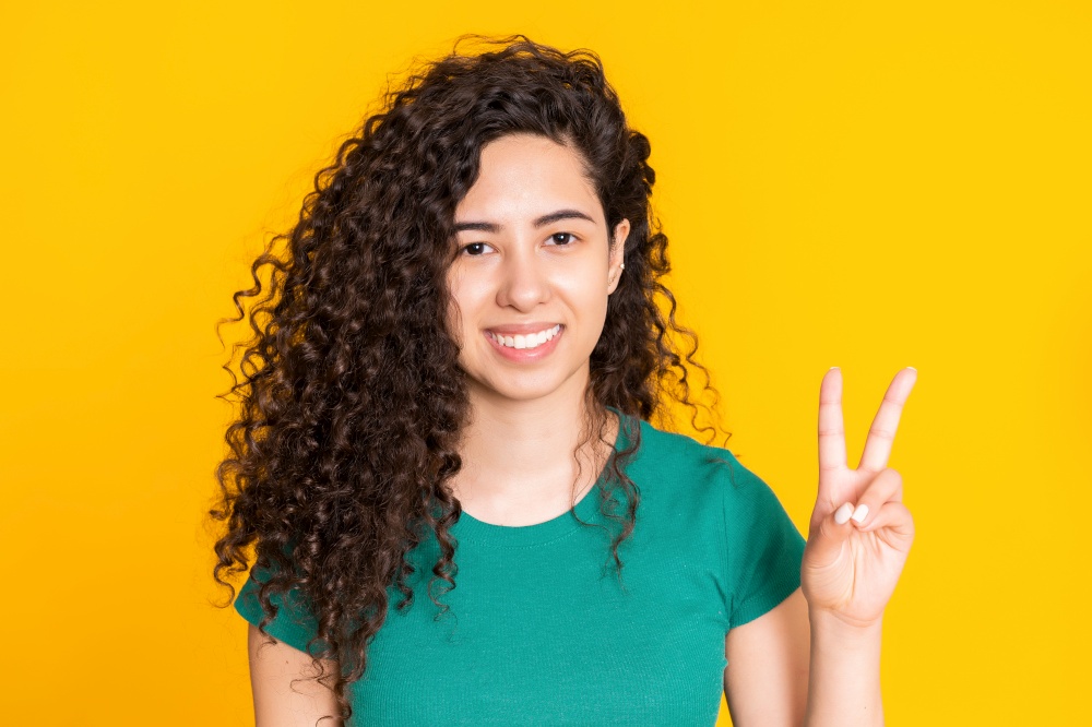 Pretty girl with curly hairstyle on yellow background. Beautiful portrait of woman in green t-shirt smiling and looking at camera. Latin or hispanic race young model.
