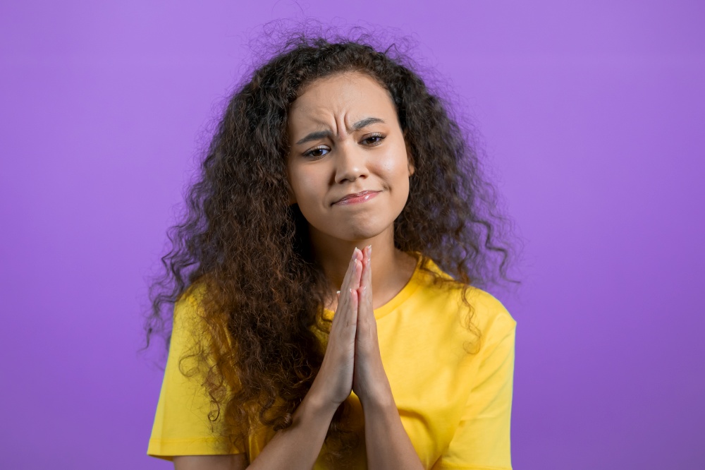 Beautiful woman praying over purple background. Girl begging someone to satisfy her desires, help with. High quality photo. Beautiful woman praying over purple background. Girl begging someone to satisfy her desires, help with.