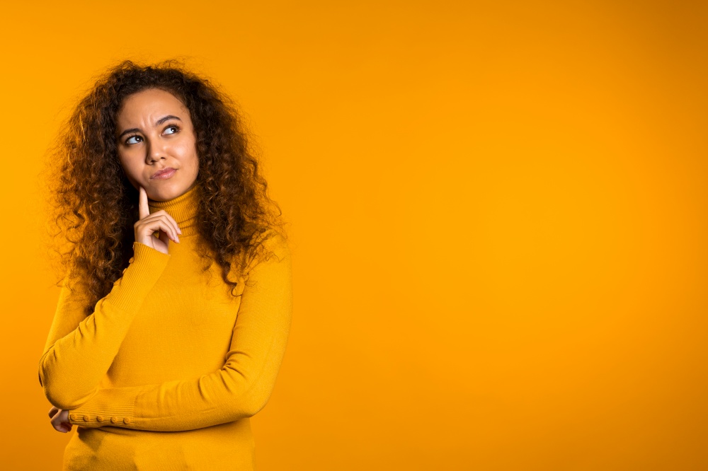 Thinking woman looking up and around on yellow background. Worried contemplative face expressions. Pretty curly girl model.. Thinking woman looking up and around on yellow background. Worried contemplative face expressions. Pretty curly girl model