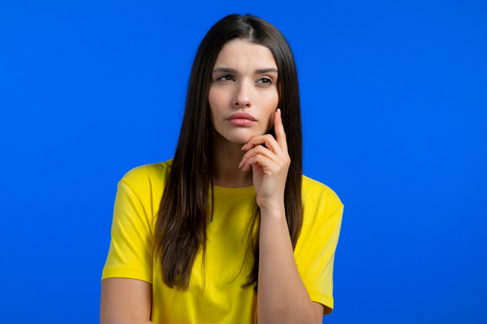 Thinking woman looking up on blue studio background. Pensive face expressions. Pretty model with attractive appearance . High quality photo. Thinking woman looking up on blue studio background. Pensive face expressions. Pretty model with attractive appearance