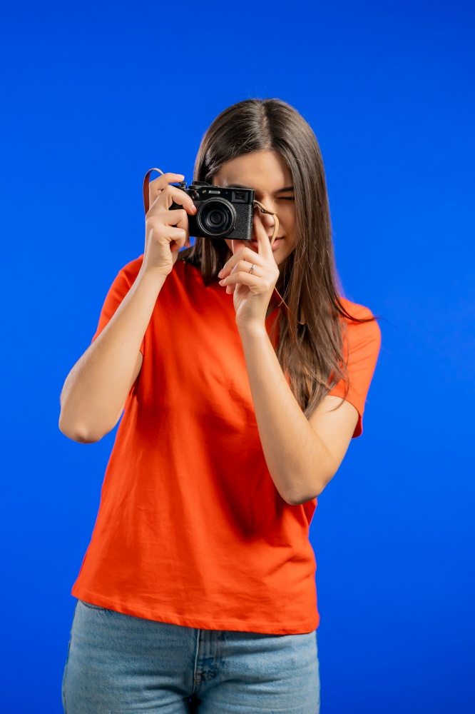 Young pretty woman takes pictures with DSLR camera over blue background in studio. Girl smiling as photographer. High quality photo. Young pretty woman takes pictures with DSLR camera over blue background in studio. Girl smiling as photographer.