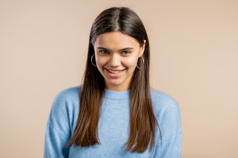 Young woman in blue sweater looking to camera, smiling. Beautiful model lady on beige studio background. Young woman in blue sweater looking to camera, smiling. Beautiful model lady on beige studio background.