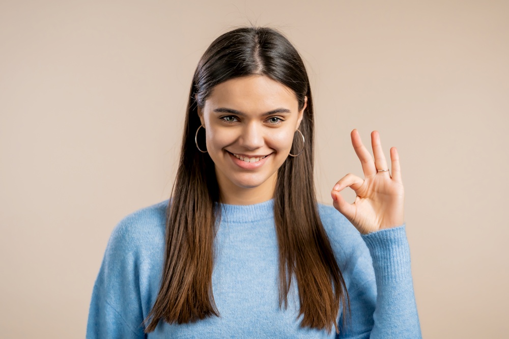Woman showing Ok sign over studio background. Positive young girl smiles to camera. Winner. Success. Body language. Woman showing Ok sign over studio background. Positive young girl smiles to camera. Winner. Success. Body language.