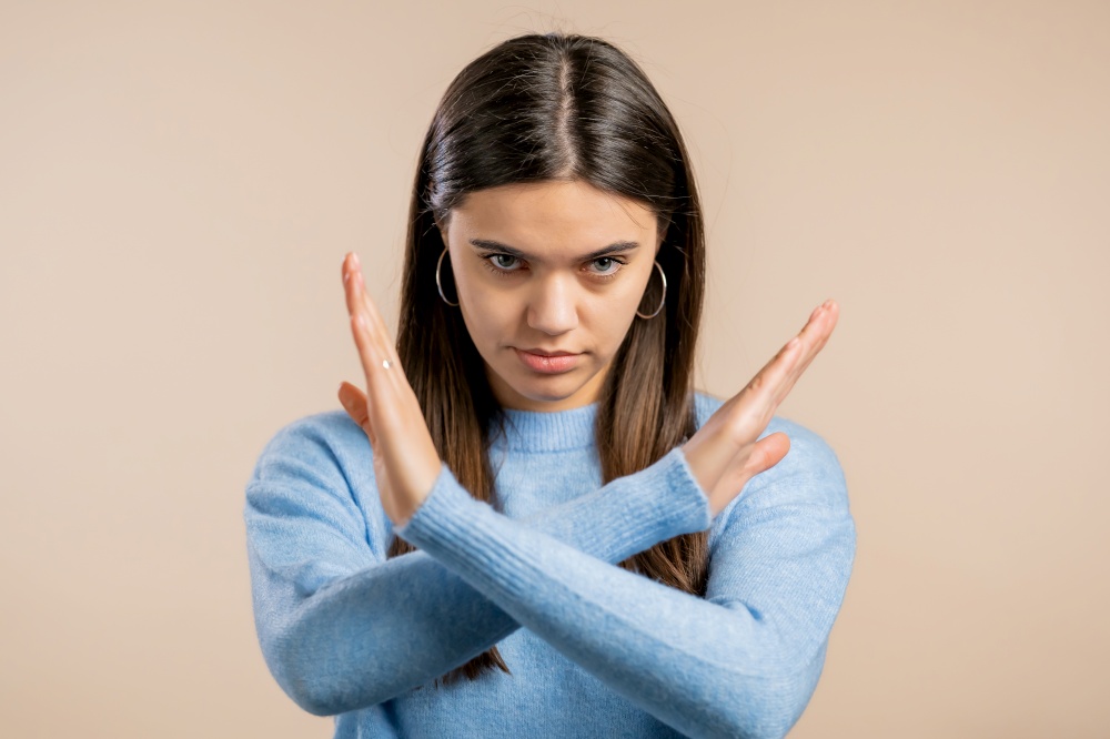 Uninterested woman disapproving with NO crossing hands sign gesture. Denying, rejecting, disagree. Portrait of young lady on blue background, timeout concept. High quality photo. Uninterested woman disapproving with NO crossing hands sign gesture. Denying, rejecting, disagree. Portrait of young lady on blue background, timeout concept.