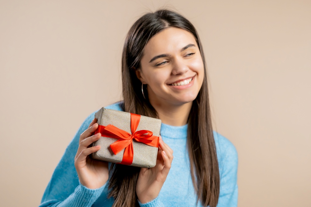Excited woman received gift box with bow. She is happy and flattered by attention. Girl smiling with present on light background. Studio portrait.. Excited woman received gift box with bow. She is happy and flattered by attention. Girl smiling with present on light background. Studio portrait