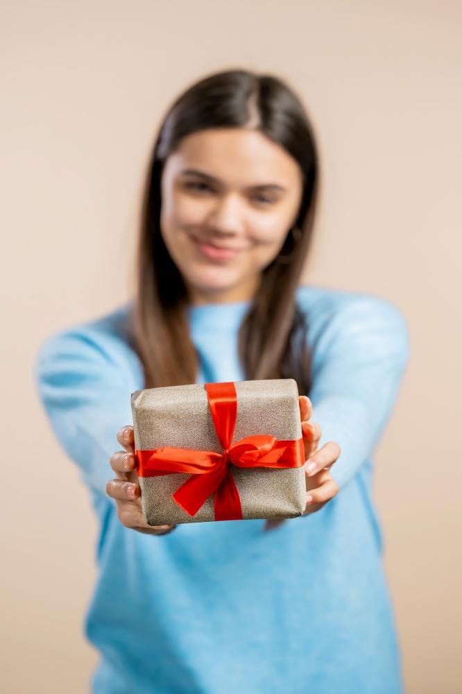 Excited woman holding gift box and gives it by hands to camera on light wall background. Girl smiling, she is happy with present. Studio portrait.. Excited woman holding gift box and gives it by hands to camera on light wall background. Girl smiling, she is happy with present. Studio portrait