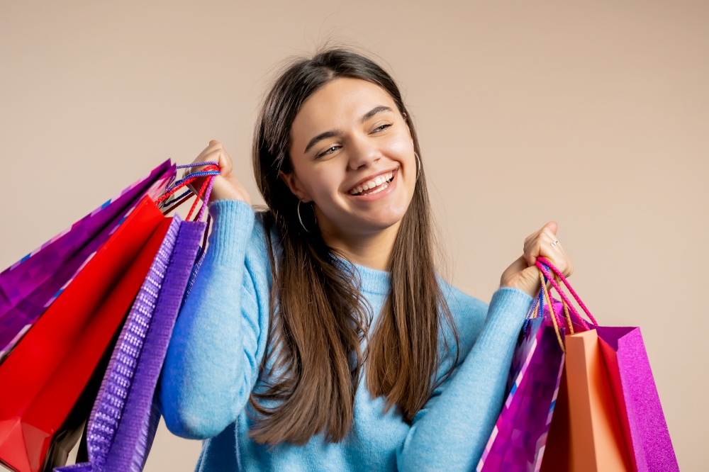 Happy woman with colorful paper bags after shopping on beige studio background. Concept of seasonal sale, purchases, spending money on gifts.. Happy woman with colorful paper bags after shopping on beige studio background. Concept of seasonal sale, purchases, spending money on gifts