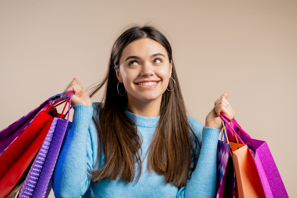 Happy woman with colorful paper bags after shopping on beige studio background. Concept of seasonal sale, purchases, spending money on gifts.. Happy woman with colorful paper bags after shopping on beige studio background. Concept of seasonal sale, purchases, spending money on gifts