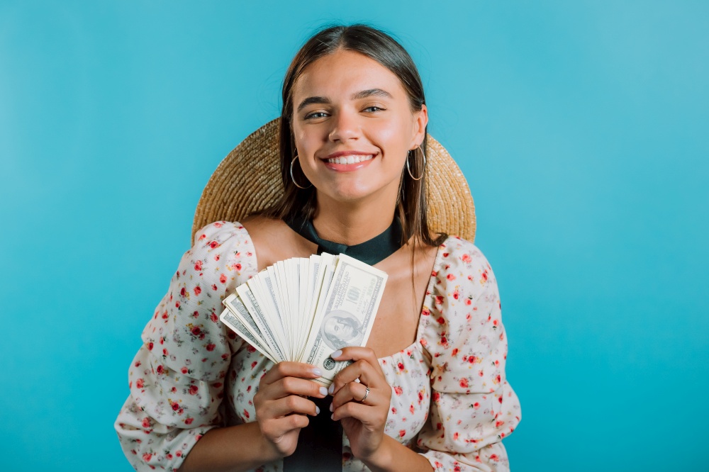 Amazed happy excited woman with money - U.S. currency dollars banknotes on blue wall. Symbol of success, gain, victory. Amazed happy excited woman with money - U.S. currency dollars banknotes on blue wall. Symbol of success, gain, victory.