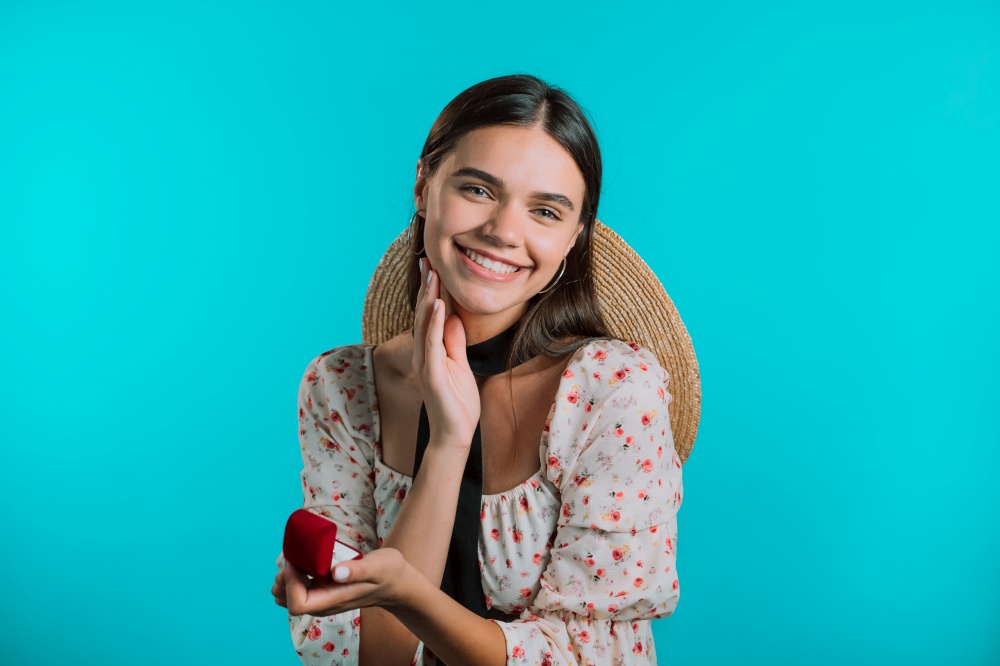 Attractive young woman holding small jewelry box with proposal diamond ring on blue wall background. Lady smiling, she is happy to get present, proposition for marriage.. Attractive young woman holding small jewelry box with proposal diamond ring on blue wall background. Lady smiling, she is happy to get present, proposition for marriage