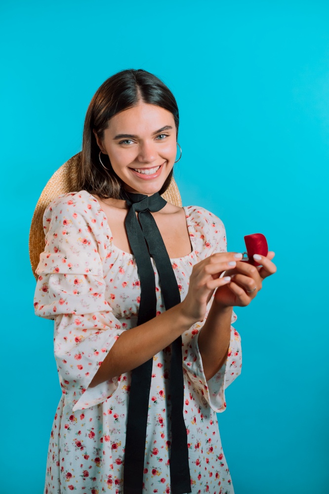 Attractive young woman holding small jewelry box with proposal diamond ring on blue wall background. Lady smiling, she is happy to get present, proposition for marriage.. Attractive young woman holding small jewelry box with proposal diamond ring on blue wall background. Lady smiling, she is happy to get present, proposition for marriage