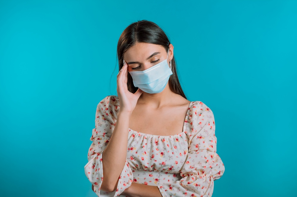 Girl in medical mask is tired, bored of work or studying, she disappointed, helpless. Frustrated european woman over blue wall background. Girl in medical mask is tired, bored of work or studying, she disappointed, helpless. Frustrated european woman over blue wall background.
