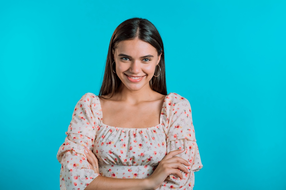 Young smiling woman looking to camera. Portrait of cute beautiful girl in floral dress on blue studio wall background. Young smiling woman looking to camera. Portrait of cute beautiful girl in floral dress on blue studio wall background.