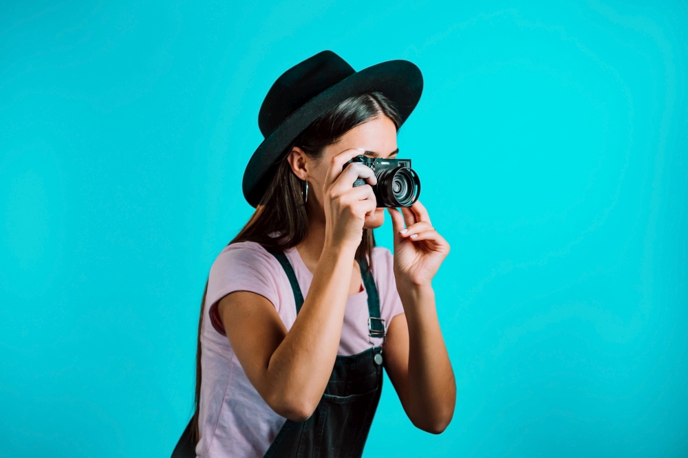Young pretty woman in overall takes pictures with DSLR camera over blue background in studio. Girl smiling and having fun as photographer. High quality photo. Young pretty woman in overall takes pictures with DSLR camera over blue background in studio. Girl smiling and having fun as photographer.
