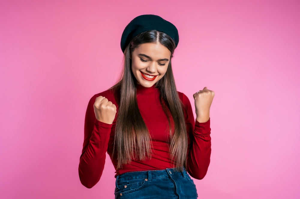 Girl with long hair and pretty appearance shows yes gesture of victory, she achieved result, goals. Surprised excited happy hipster on pink background.. Girl with long hair and pretty appearance shows yes gesture of victory