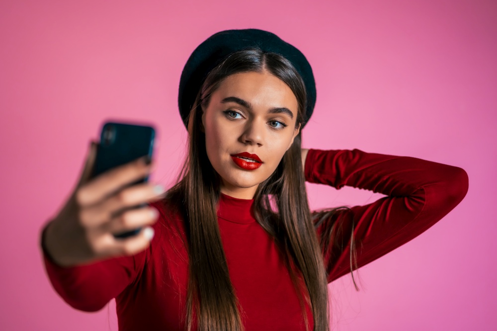 Girl with long hair and pretty appearance make selfie on pink background. Using modern technology - smartphone, social networks.. Girl with long hair and pretty appearance make selfie on pink background.