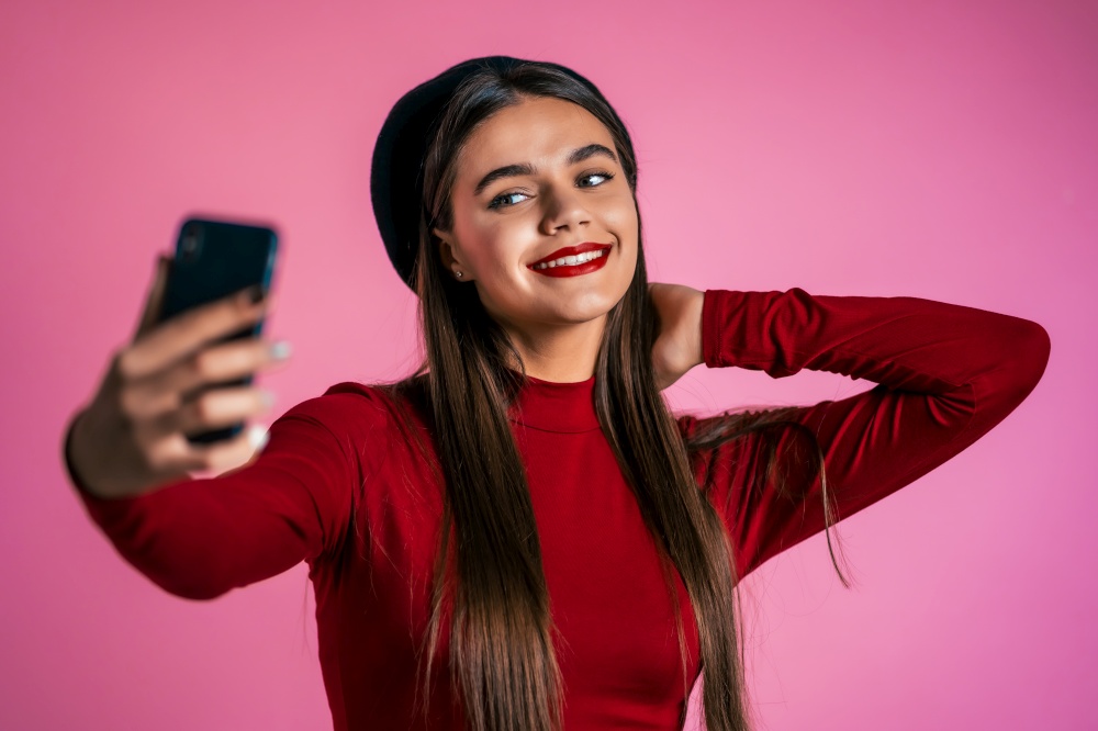 Girl with long hair and pretty appearance make selfie on pink background. Using modern technology - smartphone, social networks.. Girl with long hair and pretty appearance make selfie on pink background.