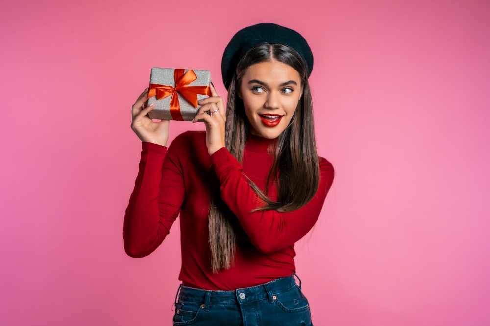 Excited woman received gift box with bow. She is happy and flattered by attention. Girl with present on pink background. Studio shot. Excited woman received gift box with bow.She is happy and flattered by attention