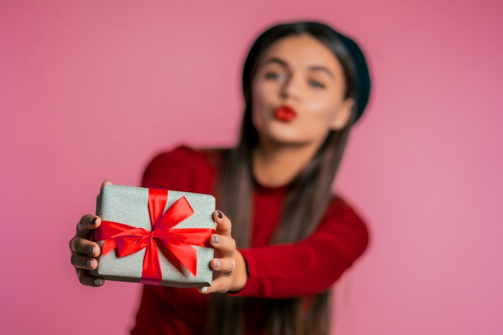 Pretty woman gives gift and hands it to the camera. She is happy, smiling. Girl on pink background. Positive holiday shot. Pretty woman gives gift and hands it to the camera. She is happy, smiling.