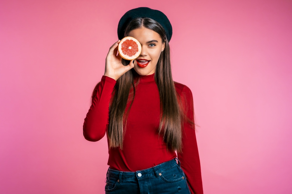 Portrait of young beautiful woman in red with two half of juicy grapefruit on pink studio background. Healthy eating, dieting, antioxidants concept. Portrait of young beautiful woman in red with two half of juicy grapefruit pink