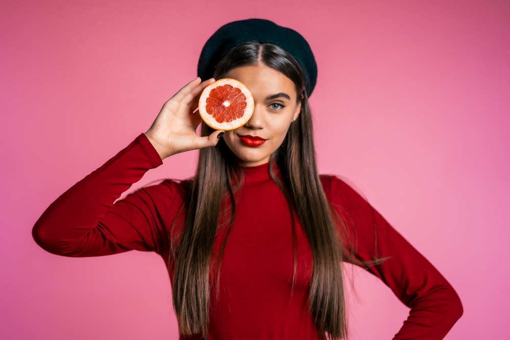 Portrait of young beautiful woman in red with two half of juicy grapefruit on pink studio background. Healthy eating, dieting, antioxidants concept. Portrait of young beautiful woman in red with two half of juicy grapefruit pink