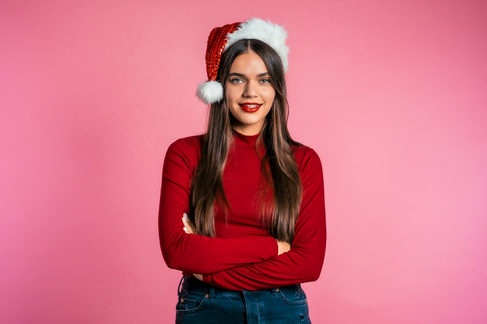 Attractive girl in Santa hat. Portrait of lady on pink background. Christmas or New year concept. Happy pretty woman smiling to camera. Attractive girl in Santa hat. Portrait of lady on pink. Christmas concept