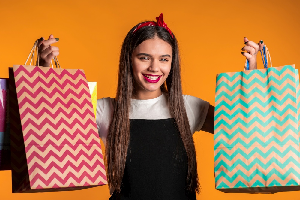 Happy young woman with long hair with paper bags after shopping isolated on yellow studio background. Seasonal sale, purchases, spending money on gifts concept.. Happy young woman with long hair with paper bags after shopping isolated on yellow studio background. Seasonal sale, purchases, spending money on gifts concept
