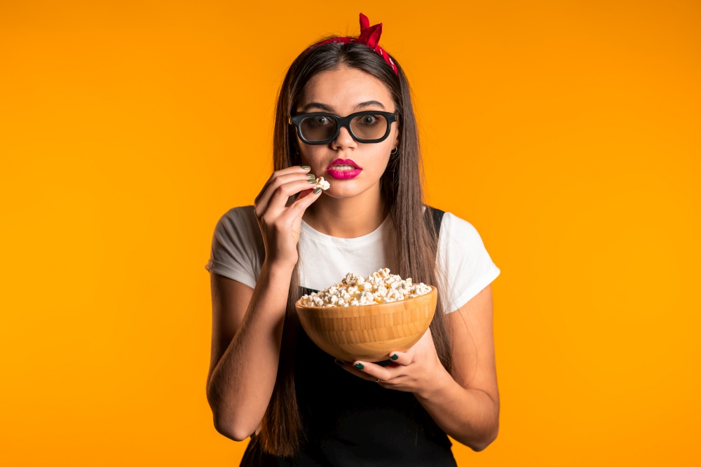 Young woman in 3d glasses watching horror movie and eating popcorn on yellow studio background. Young woman in 3d glasses watching horror movie and eating popcorn on yellow studio background.