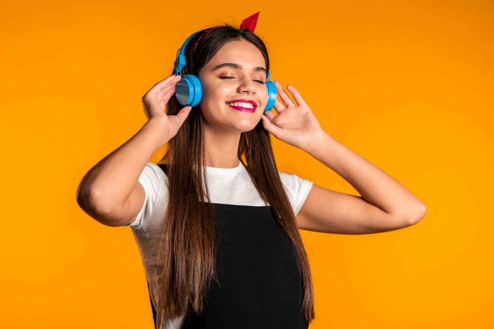 Pretty young girl with long hair having fun, smiling, dancing with headphones in studio against yellow background. Music, dance, radio concept. Pretty young girl with long hair having fun, smiling, dancing with headphones in studio against yellow background. Music, dance, radio concept,