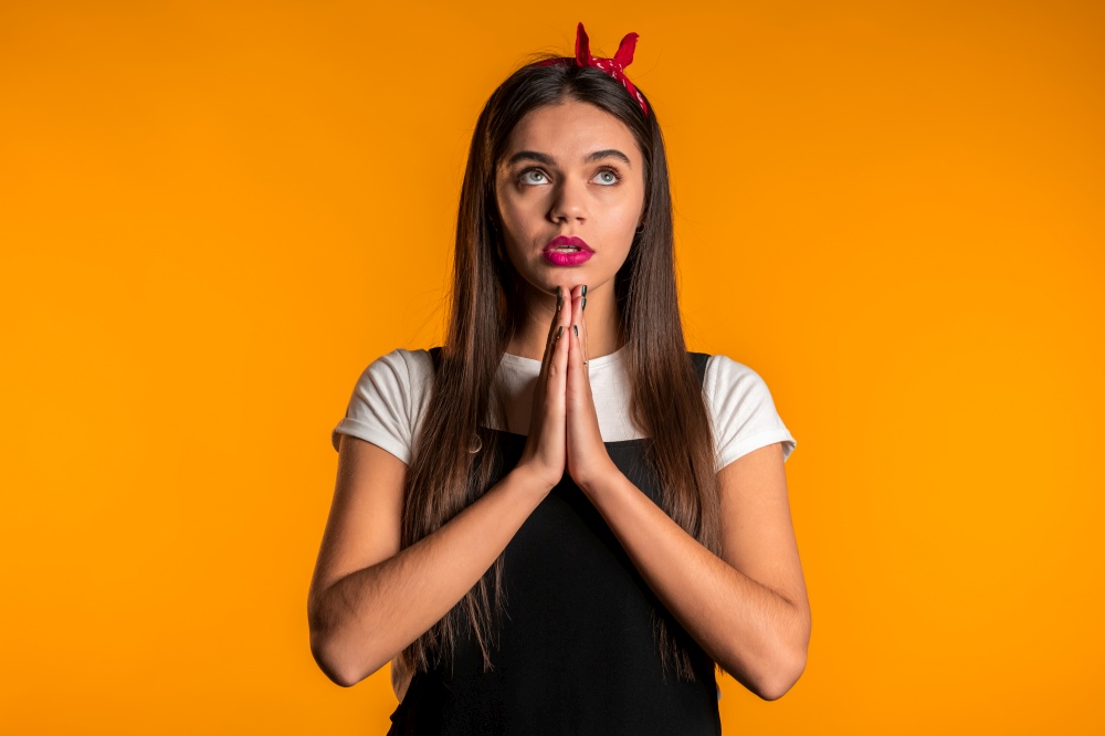 Cute young girl with beautiful hairstyle praying over yellow background. Woman begging someone. Cute young girl with beautiful hairstyle praying over yellow background. Woman begging someone.