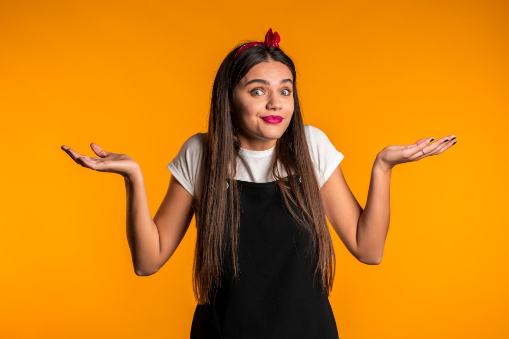 Young unsure girl shrugs her arms, makes gesture of I don&rsquo;t know, care, can&rsquo;t help anything .Young millenial woman on yellow background..  Young unsure girl shrugs her arms, makes gesture of I don&rsquo;t know, care, can&rsquo;t help anything .Young millenial woman on yellow background