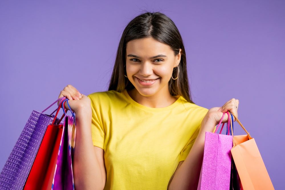 Excited woman with colorful paper bags after shopping on violet studio background. Concept of seasonal sale, purchases, spending money on gifts.. Excited woman with colorful paper bags after shopping on violet studio background. Concept of seasonal sale, purchases, spending money on gifts