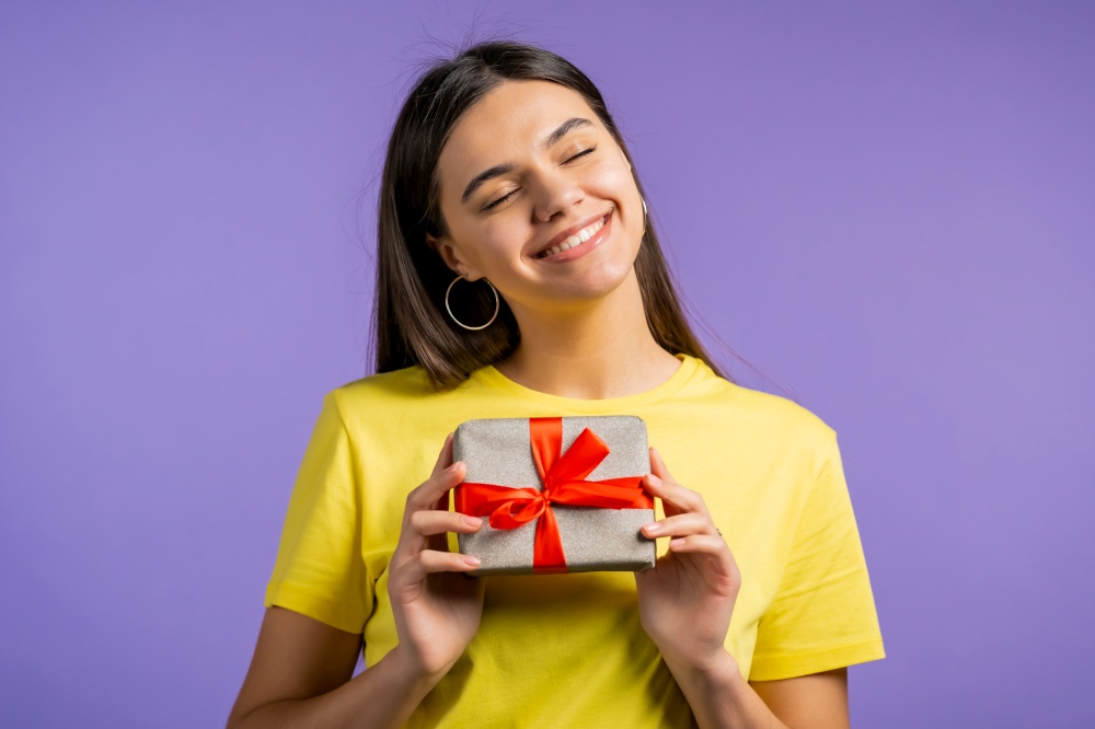 Beautiful woman received gift box with bow. She is happy and flattered by attention. Girl smiling with present on violet background. Studio portrait.. Beautiful woman received gift box with bow. She is happy and flattered by attention. Girl smiling with present on violet background. Studio portrait