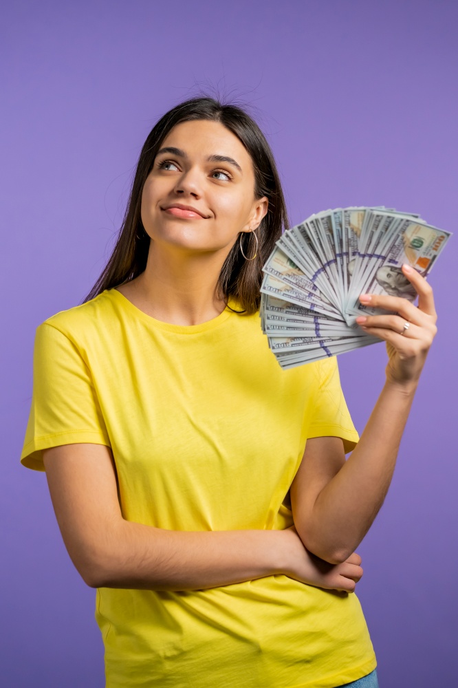 Smiling happy woman with cash money - USD currency dollars banknotes on violet wall. Symbol of jackpot, gain, victory, winning the lottery.. Smiling happy woman with cash money - USD currency dollars banknotes on violet wall. Symbol of jackpot, gain, victory, winning the lottery