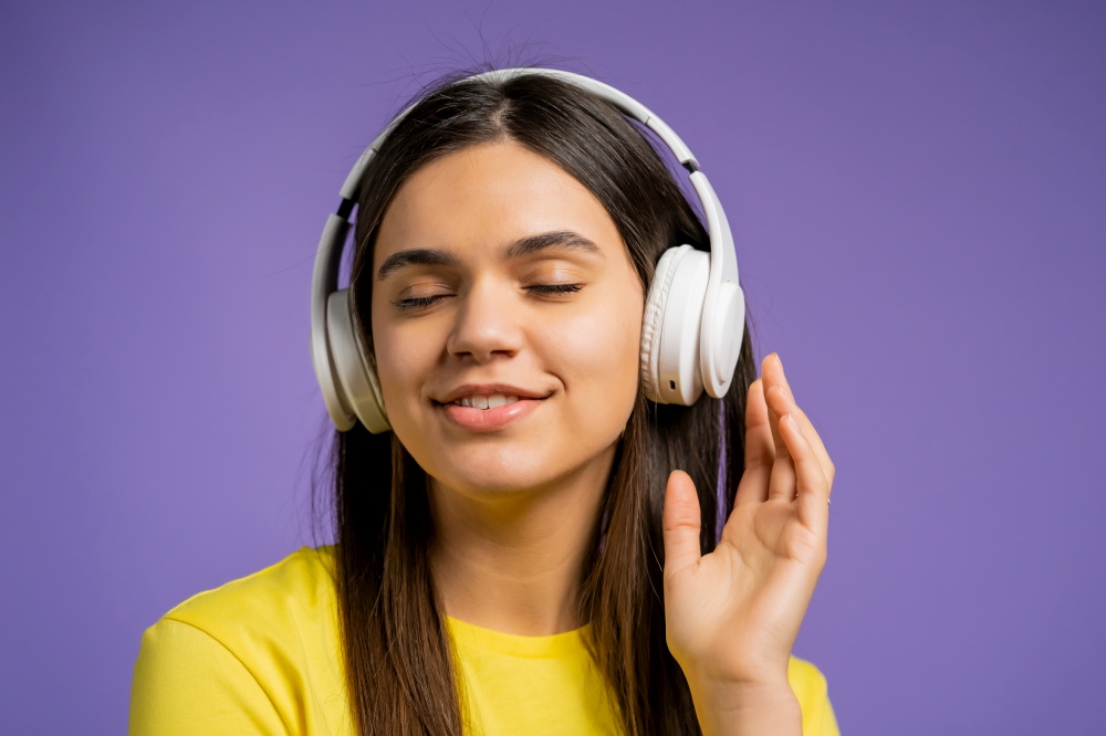 Attractive woman with white headphones on violet studio background. Cute girls portrait. Music, radio, happiness, freedom, youth concept. Attractive woman with white headphones on violet studio background. Cute girls portrait. Music, radio, happiness, freedom, youth concept.