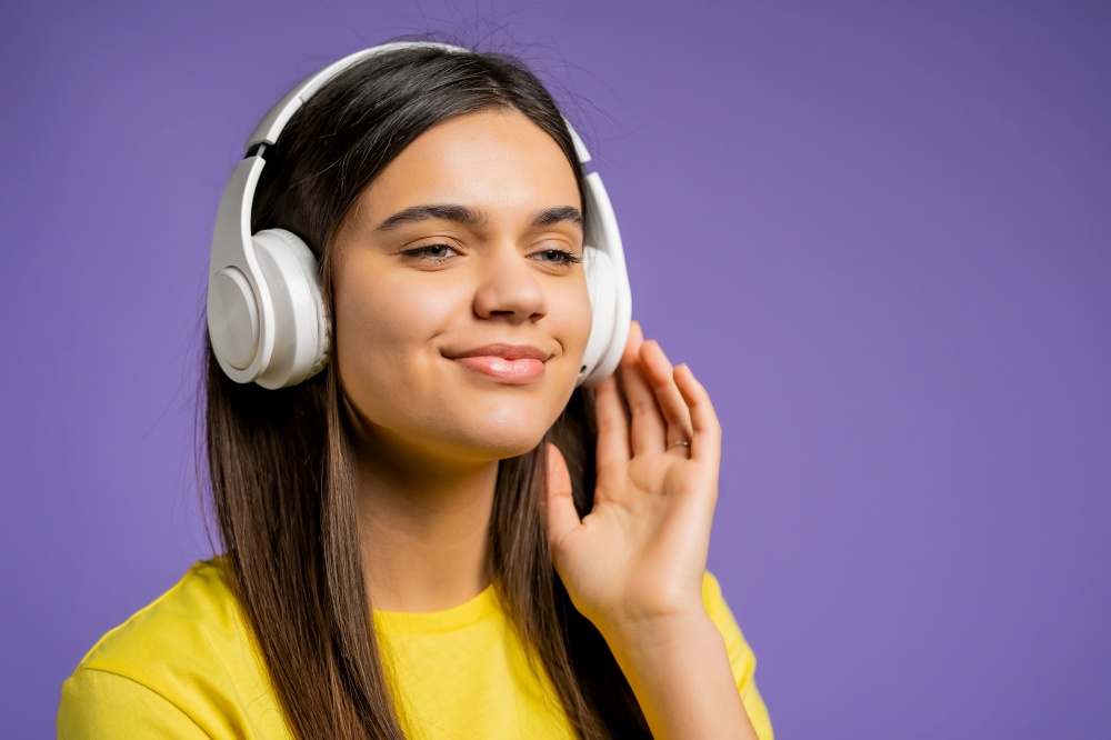 Attractive woman with white headphones on violet studio background. Cute girls portrait. Music, radio, happiness, freedom, youth concept. Attractive woman with white headphones on violet studio background. Cute girls portrait. Music, radio, happiness, freedom, youth concept.