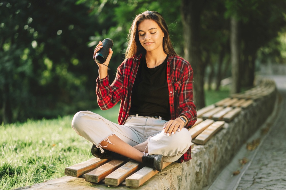 Modern trendy girl listening to music by wireless portable speaker.Young beautiful american woman enjoying,dancing in park. Modern trendy girl listening to music by wireless portable speaker.Young beautiful american woman enjoying,dancing in park.