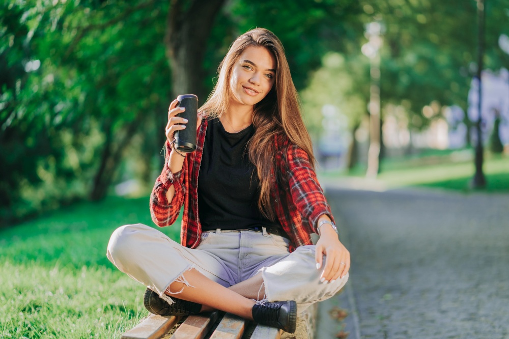 Modern trendy girl listening to music by wireless portable speaker.Young beautiful american woman enjoying,dancing in park. Modern trendy girl listening to music by wireless portable speaker.Young beautiful american woman enjoying,dancing in park.